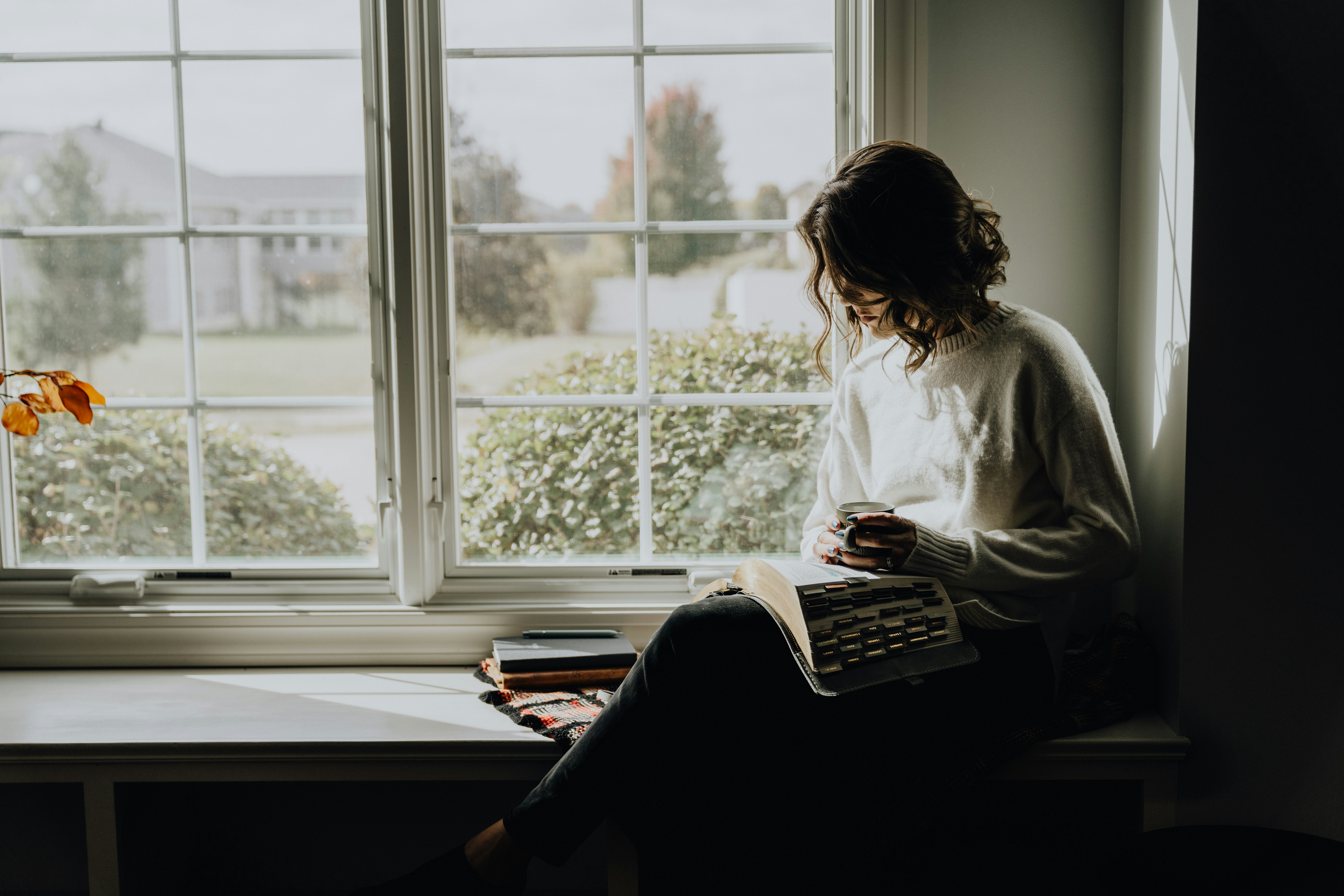 A woman sitting on a window sill reading a book